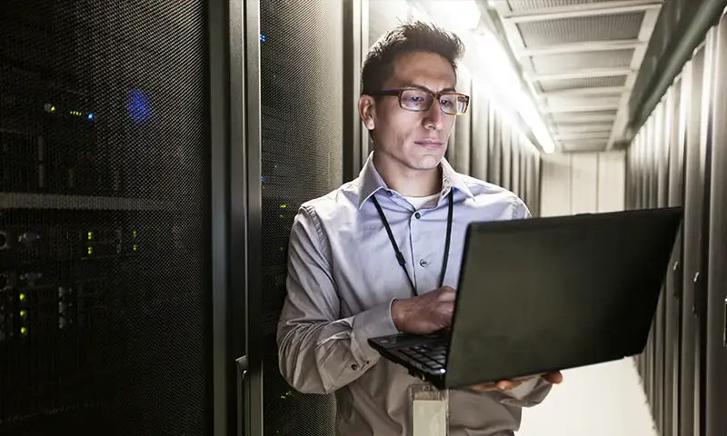 IT professional in a data center reviewing server diagnostics on a laptop